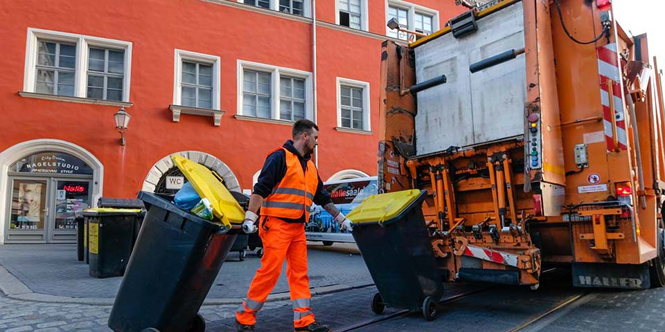 Mitarbeiter bringt zwei Mülltonnen zum Müllwagen.