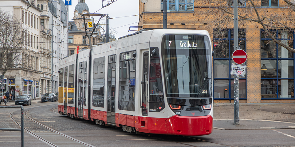 Straßenbahn der Linie 7 mit Zielanzeige Kröllwitz fährt durch eine Stadtstraße mit historischen Gebäuden.