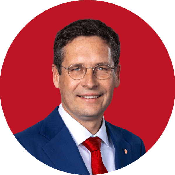 Mann in blauem Anzug und roter Krawatte vor rotem Hintergrund.
