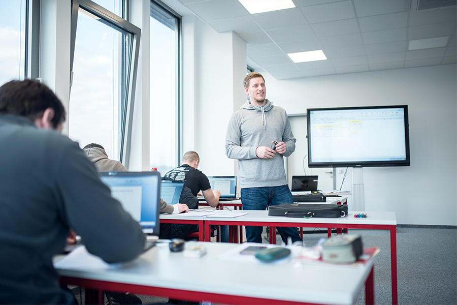 Ein Ausbilder vermittelt den Auszubildenden Wissen in einem Schulungsraum. Der Unterricht findet mit digitalen Hilfsmitteln statt