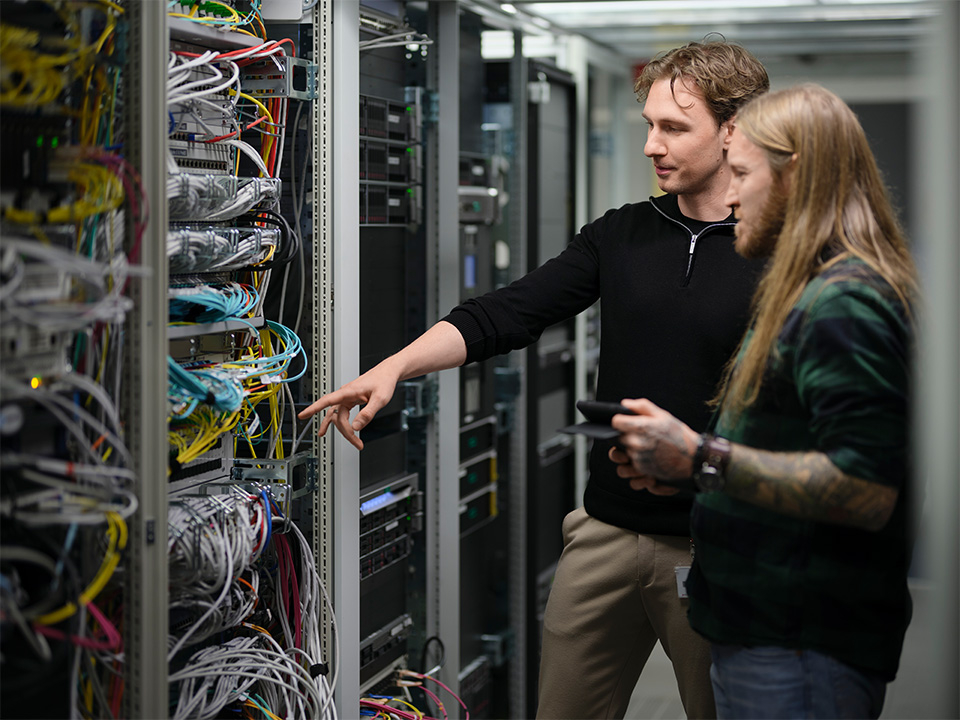 Zwei Mitarbeiter stehen vor einem offenen Serverschrank.