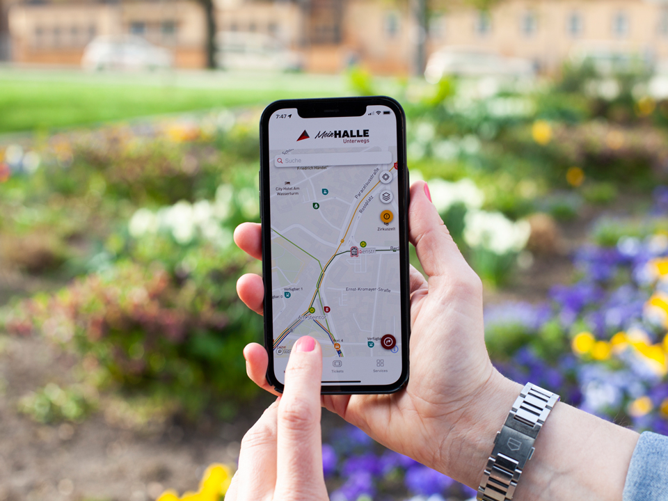 Eine Nahaufnahme eines Smartphones, welches die App Mein HALLE Unterwegs zeigt.