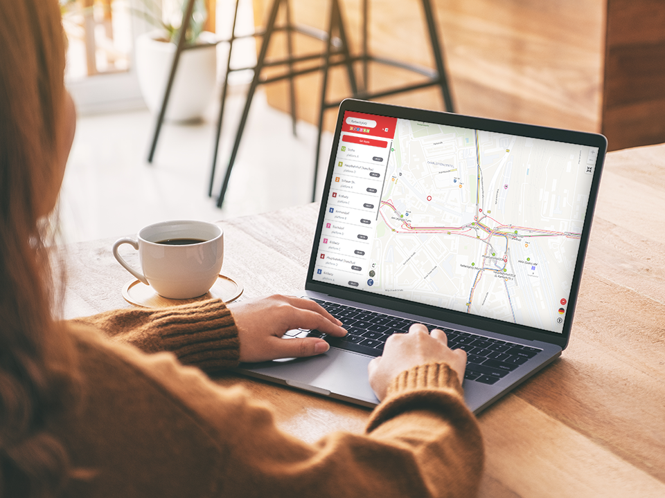 Person mit braunem Pullover bedient Laptop mit der Mobile M.app: ein hallescher Stadtplan und Haltestellen auf dem Bildschirm neben weißer Kaffeetasse auf Holztisch