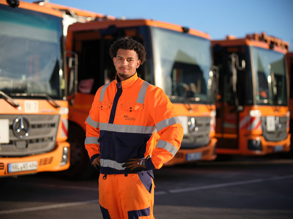 Person in orange-blauer Warnschutzkleidung steht vor einer Reihe orangefarbener Müllfahrzeuge.