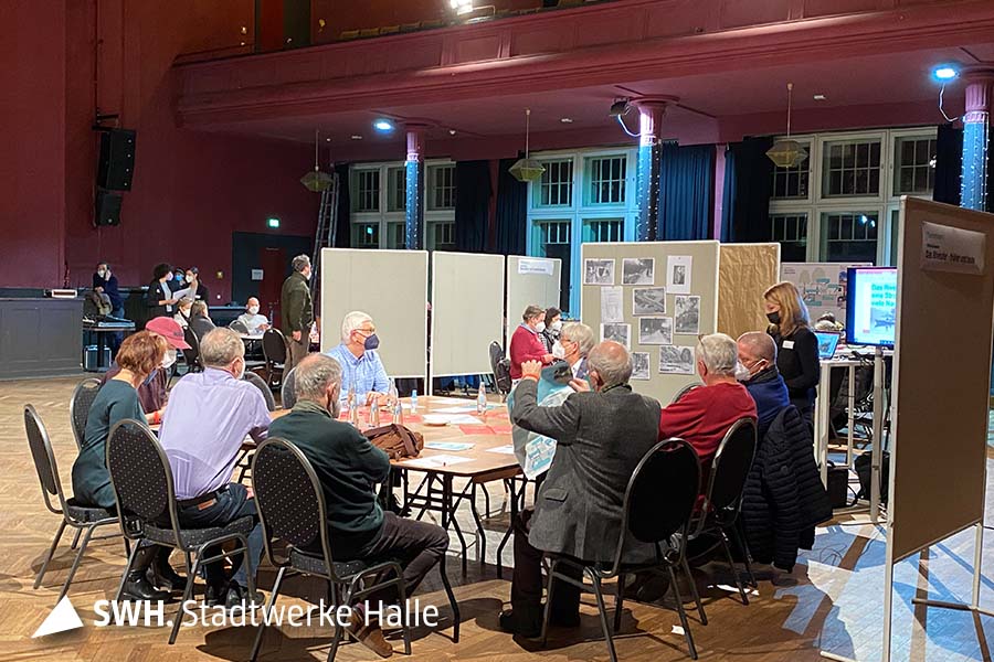 Menschen sitzen an thematisch angeordneten Tischen und besprechen die neue Ausgestaltung des Riveufers in Halle (Saale)