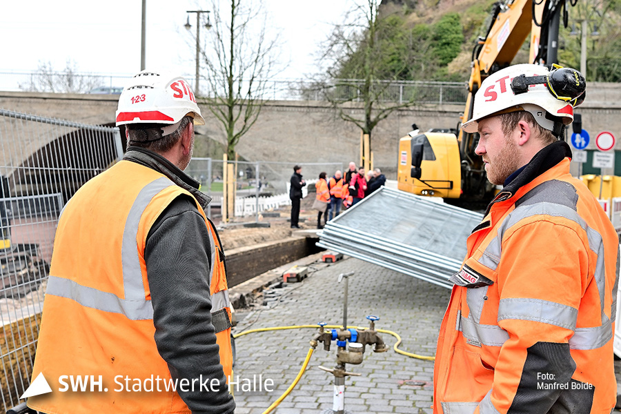 Zwei Herren sprechen miteinander, im Hintergrund ist eine Gruppe zu sehen, die sich die Baustelle am Riveufer in Halle anschaut.