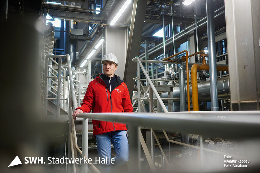 Maximilian Lohr ist mit Arbeitskleidung und Schutzhelm ausgerüstet,  in einer Industrieanlage unterwegs.