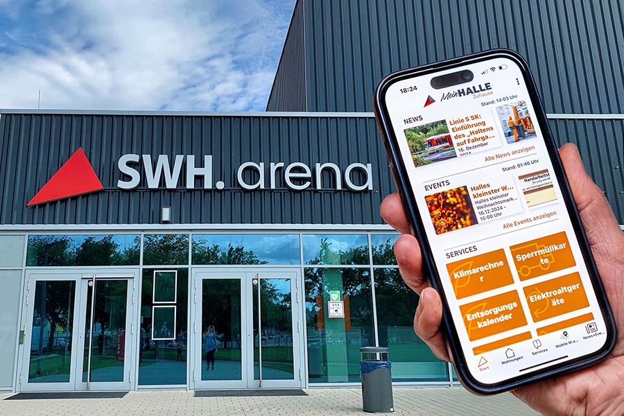 Ein Smartphone mit der geöffneten App "Mein Halle Zuhause" ist zu sehen. Im Hintergrund ist die SWH-Arena.