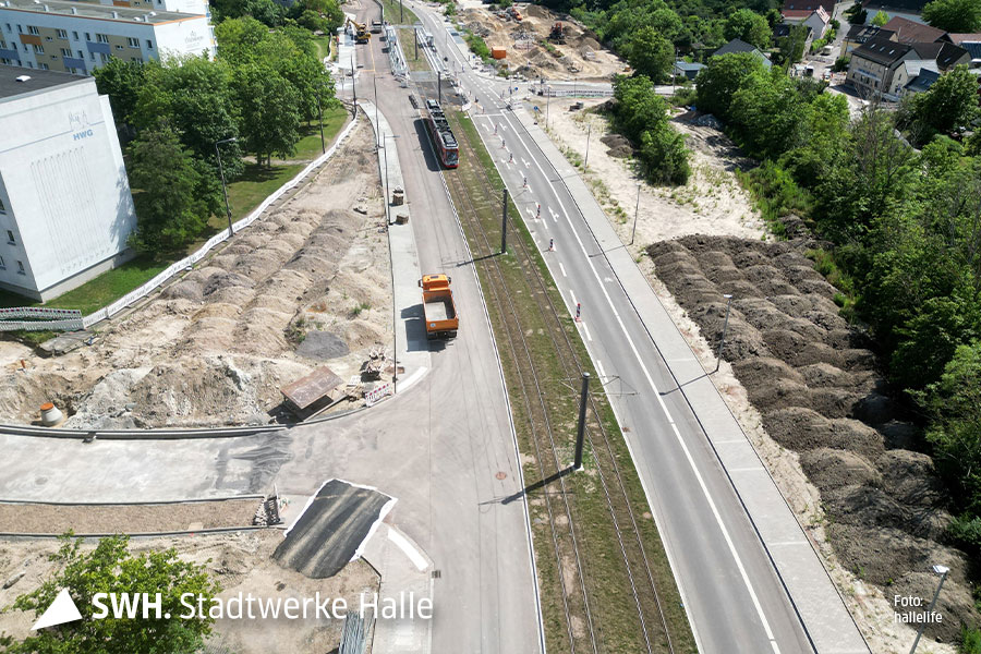 Eine Drohnenaufnahme der Kreuzung. Auf der linken Fahrspur sind noch baufahrzeuge zu sehen. Recht daneben sind zwei Straßenbahngleise. Auf einem Gleis fährt eine Straßenbahn. Rechts daneben ist die stadtauswärtige Fahrspur.