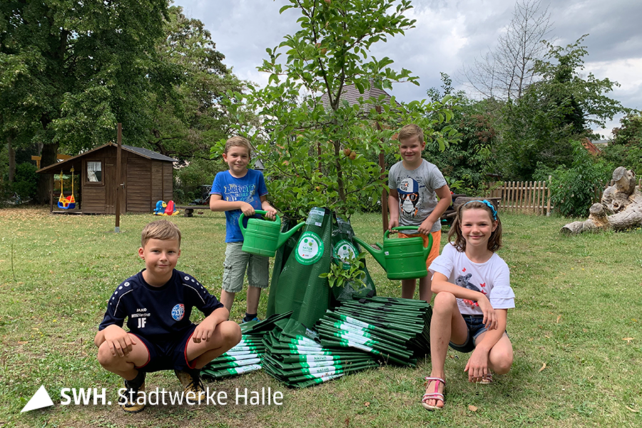 Vier Kinder stehen um einen jungen Baum und füllen Bewässerungssäcke, die an diesem Baum angebracht sind.