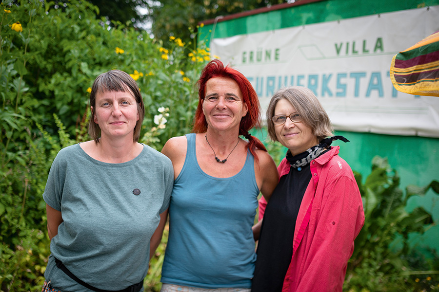 Das Foto zeigt das Portrait dreier Frauen, die vor einem Transparent mit der Aufschrift "Grüne Villa" stehen.