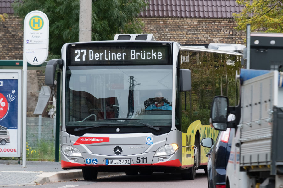 Ein silberner Bus der Marke Mercedes der Linie steht an einer Haltestelle. Die Zielaufschrift heißt "27 Berliner Brücke".