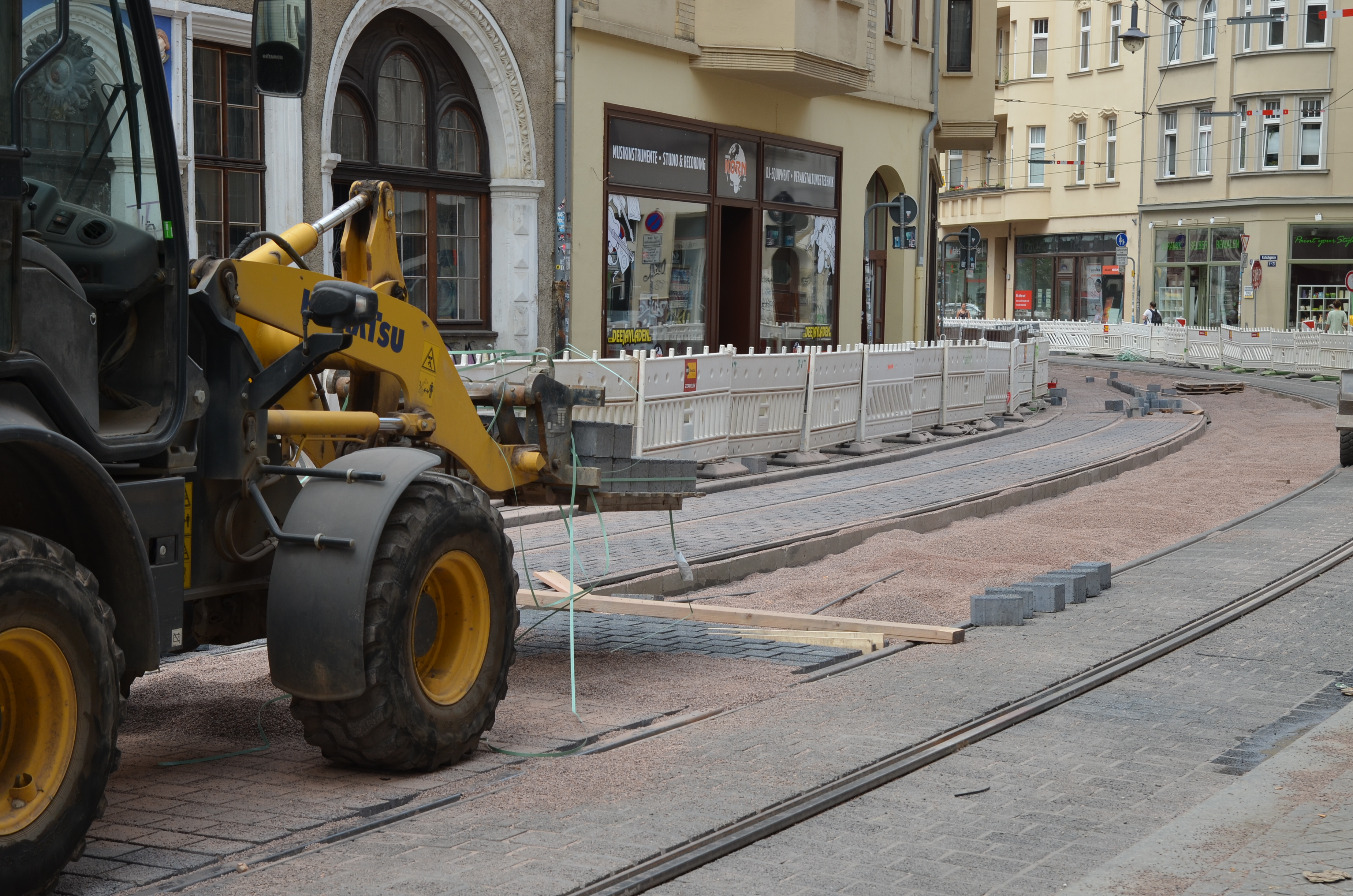 Das Foto zeigt den weiteren Verlauf der Rannischen Straße. Links im Bild ist ein gelbes Baustellenfahrzeug abgebildet, rechts die Straße mit neuen Gleisen und teilweise neuem Pflaster.
