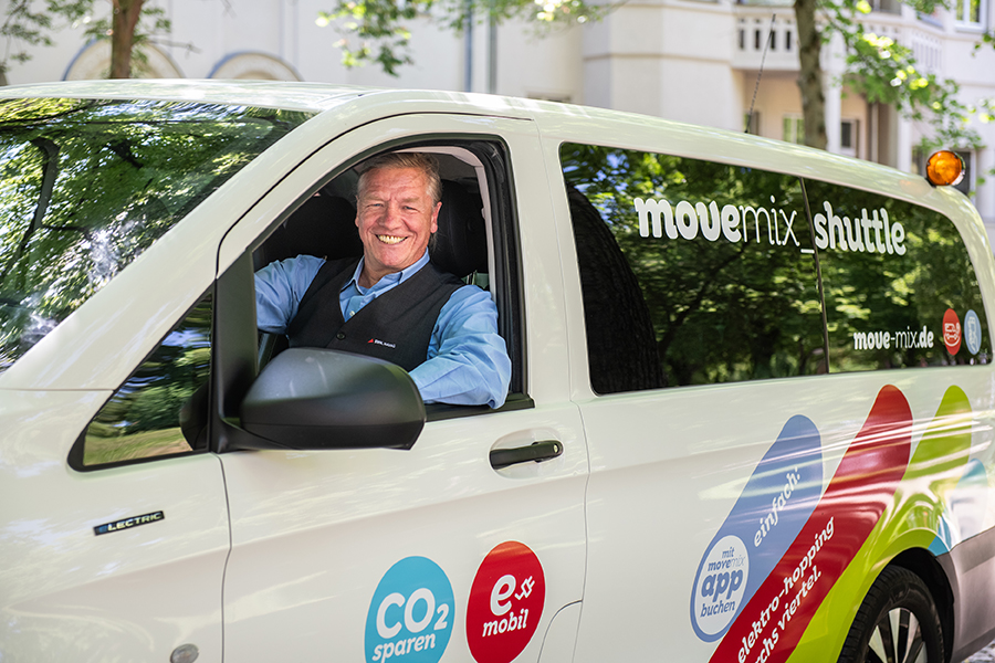 Ein Fahrer sitzt lachend am Lenkrad eines Kleinbusses -  dem movemix-shuttle.