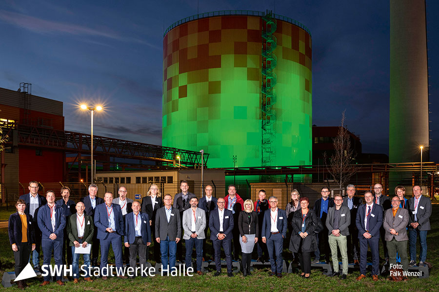 Neunundzwanzig Personen stehen im Dunkeln vor dem Energiespeicher in Halle (Saale) und schauen direkt in die Kamera für ein Foto.