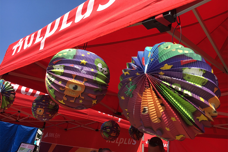 Zwei Laternen Lampions hängen vor einen Info-Stand der Stadtwerke Halle auf dem Laternenfest. Die Lampions haben kleine illustierte Monster aufgedruckt.