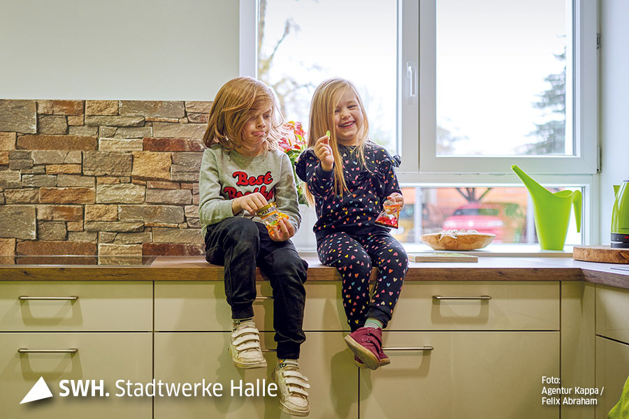 Zwei Kinder sitzen auf einem Küchentresen. Beide haben eine Gummibärchen-Tüte in der Hand.