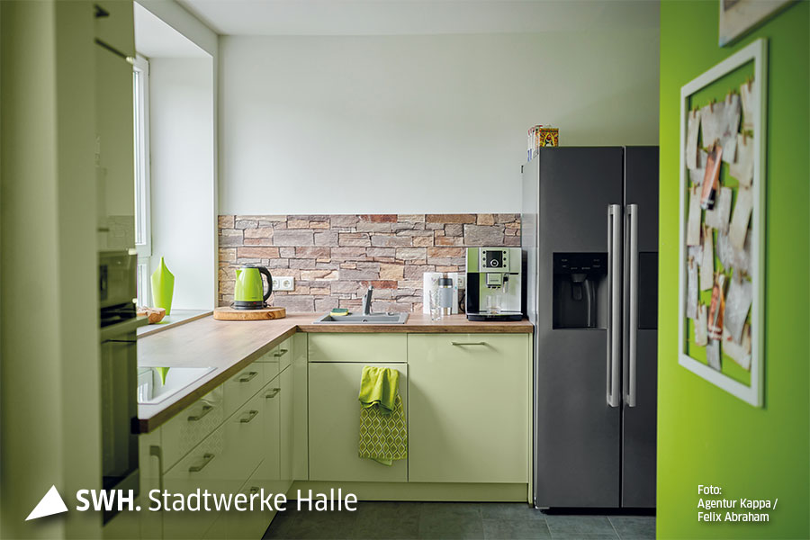 Das bild zeigt die Küche. Sie ist hellgrün. Eine Wand ist einem kräftigen Grün gestrichen. Außerdem ist ein Side-by-side-Kühlschrank zu sehen. Auch alle Utensilien wie Handtücher oder Wasserkocher sind in grün.