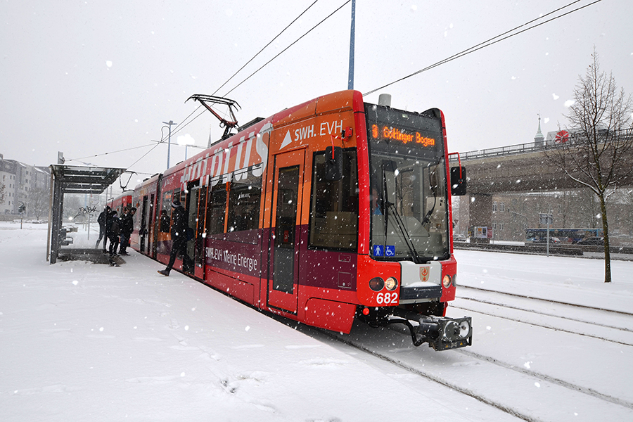 Eine bunt-beklebte Straßenbahn der HAVAG an einer Haltestelle- Fahrgäste steigen aus. Es schneit.