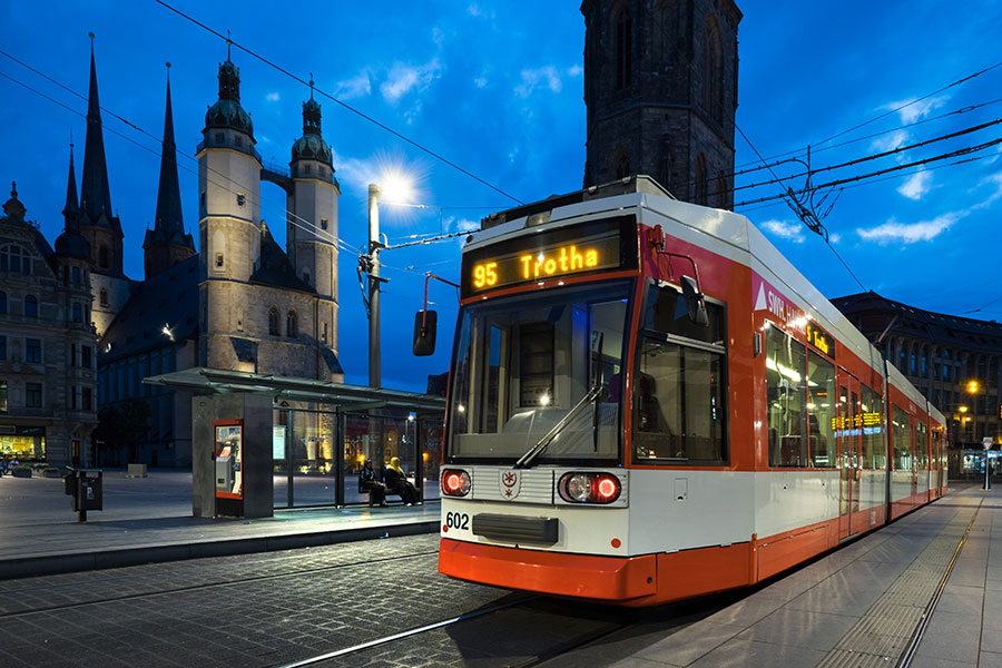 Eine Nachtaufnahme der roten Straßenbahn auf dem Markt. Die Zielaufschrift lautet "95 Trotha". Im Hintergrund ist die Kirche und eine Haltestelle zu sehen.