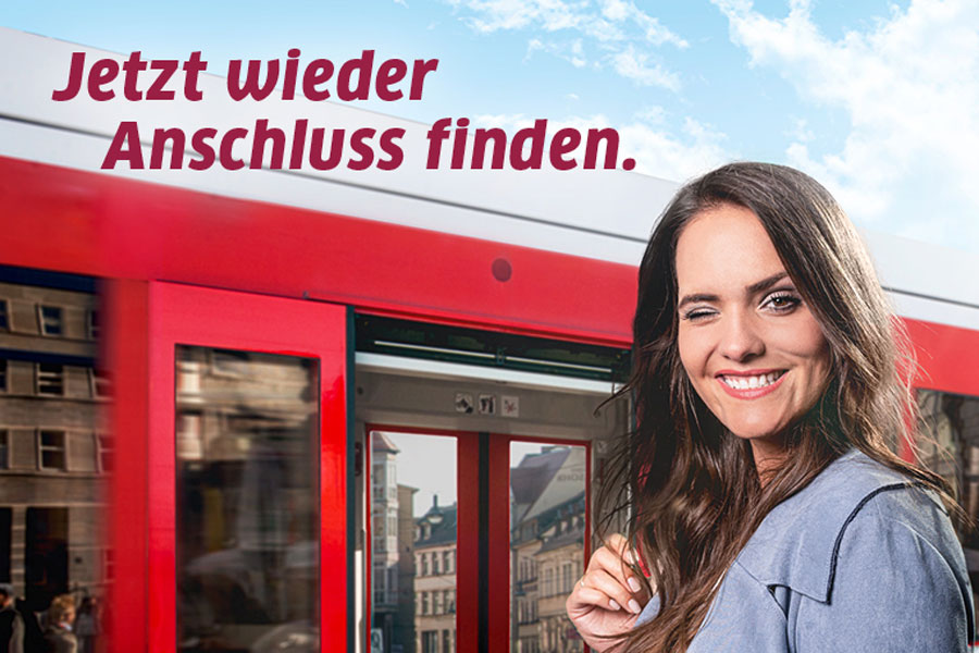 Die Grafik zeigt eine Frau mit braunen, leicht gelockten Haaren, die zwinkernd vor einer roten Straßenbahn steht. Der Himmel ist blau mit leichten Wolken. Die Tür der Straßenbahn ist geöffnet. Darüber steht der Name der Aktion "Jetzt wieder Anschluss finden".