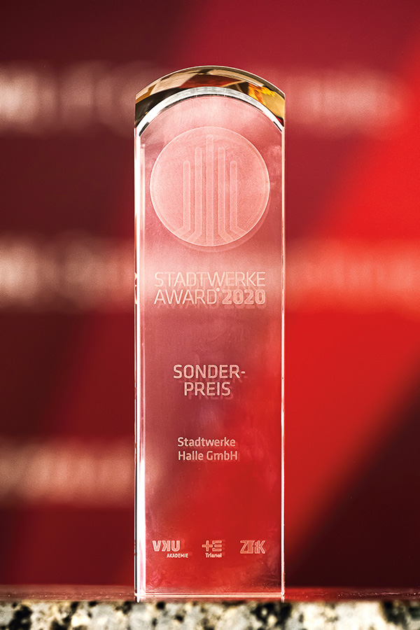 Das Foto zeigt eine gläserne Trophäe mit der Aufschrift "Stadtwerke Award 2020", "Sonderpreis" und "Stadtwerke Halle GmbH". Das Foto wurde vor einer roten Wand aufgenommen.