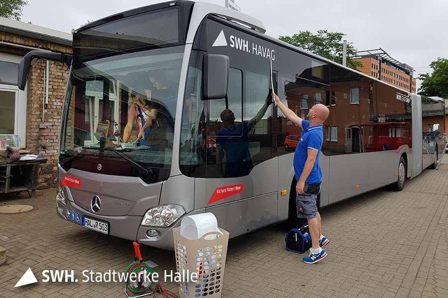 Ein Mann steht an einem stehenden Bus, zwei Männer sind in der Fahrerkabine zu sehen.