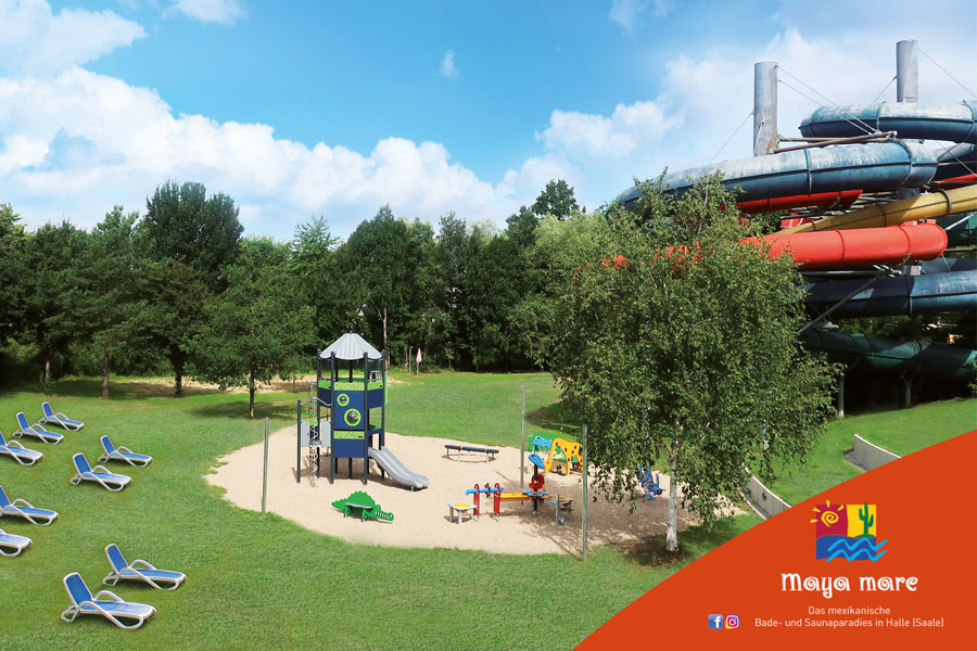 Das Bild zeigt den neuen Kinderspielplatz. In der Mitte steht ein Klettergerüst im Sand. Daneben stehen Liegen und ein schattenspendender Baum. Im Hintergrund sind die Rutschen des Maya mare zu sehen.