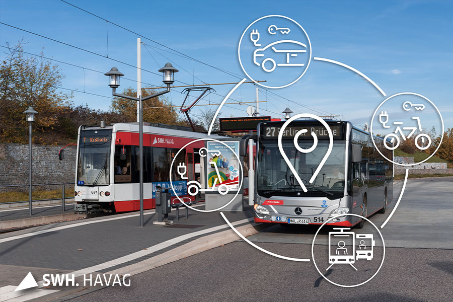 Eine rote Straßenbahn der HAVAG (Linie 7) steht an der Haltestelle in Büschdorf. Rechts daneben ist die Haltestelle mit einer optischen Fahrgastanzeige. Rechts daneben steht ein silberner Bus (Linie 27) der HAVAG. Der Himmel ist strahlend blau und wolkenlos.