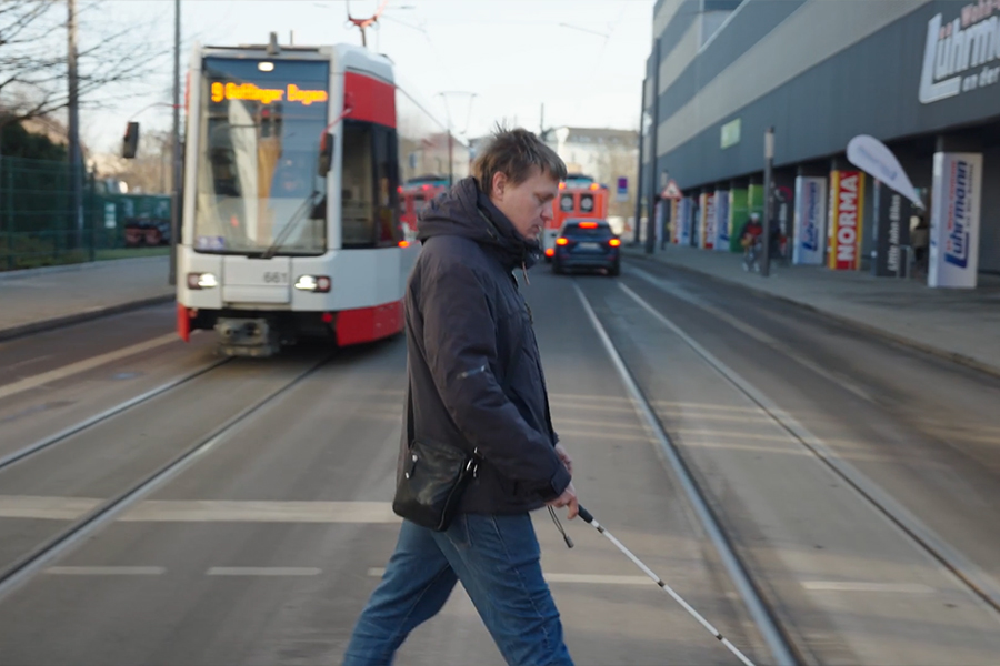 Sehbehinderter Mann überquert eine Straße mit Ampelsystem