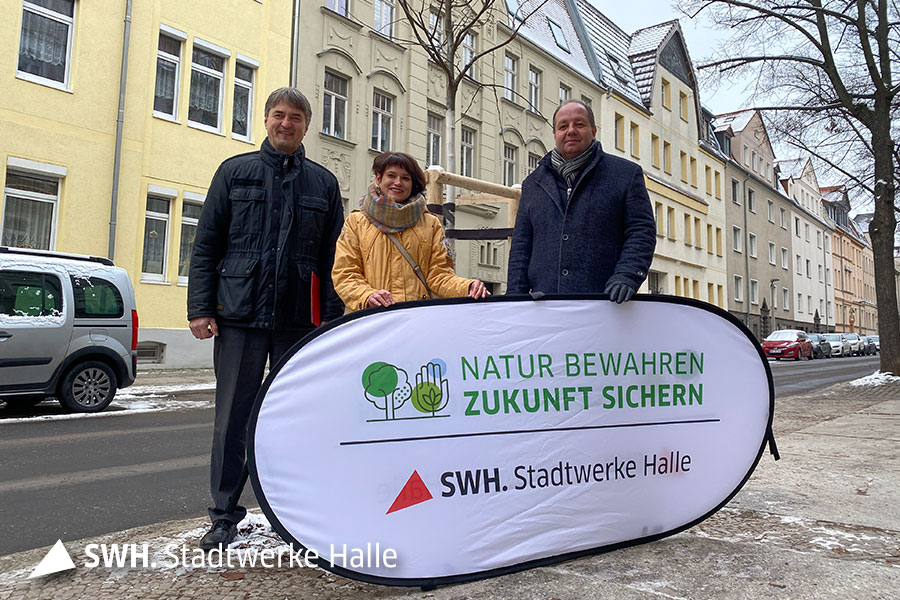 Zwei Männer und eine Frau halten ein Banner in die Kamera zur Baumpflanzaktion der Stadtwerke Halle GmbH.