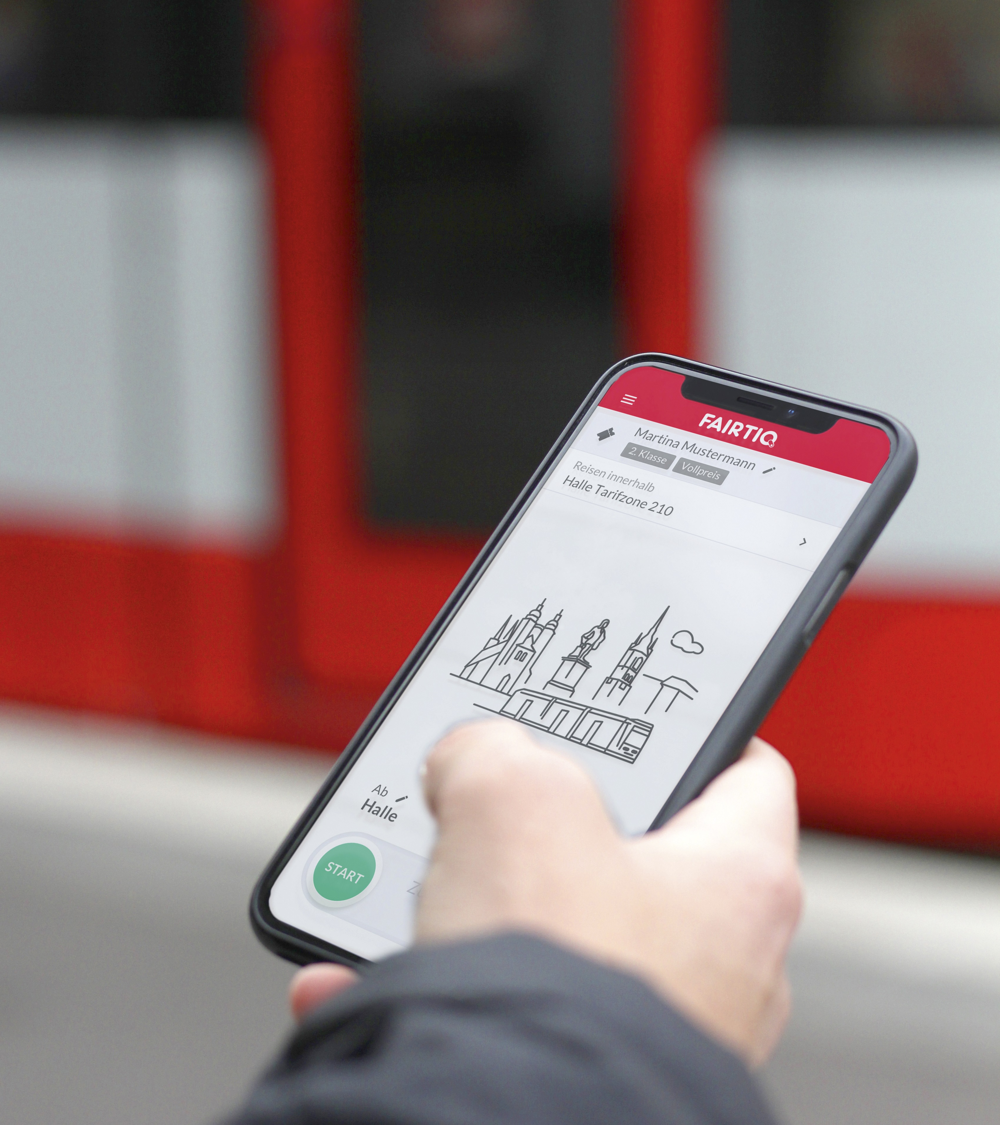 Auf dem Foto befindet sich mittig ein Smartphone, dessen Bildschirm die Startseite von "FAIRTIQ" angezeigt wird. Das Smartphone wird von einer Hand gehalten und im Hintergrund befindet sich eine rote Straßenbahn.