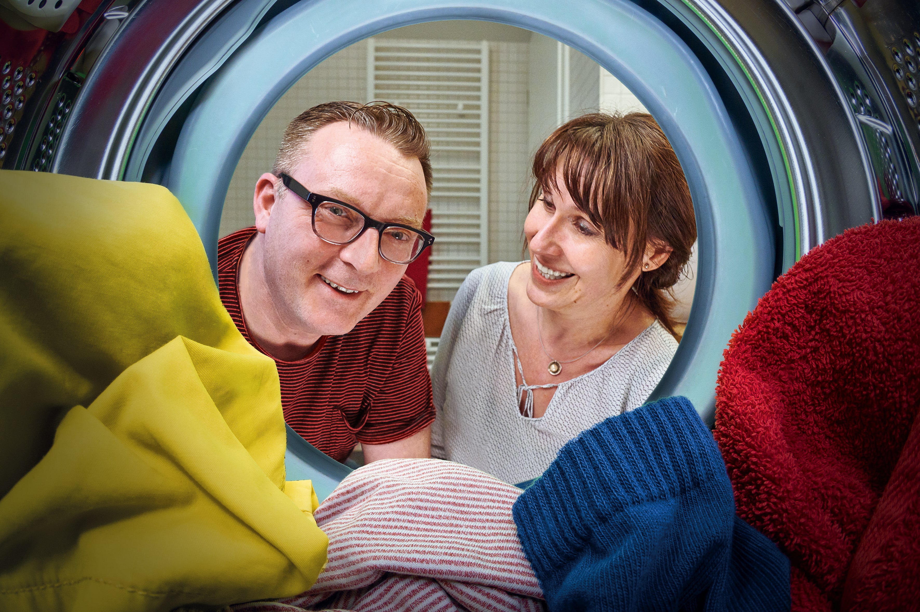 Ein Mann und eine Frau schauen symbolisch durch eine neue Waschmaschine in die Zukunft.