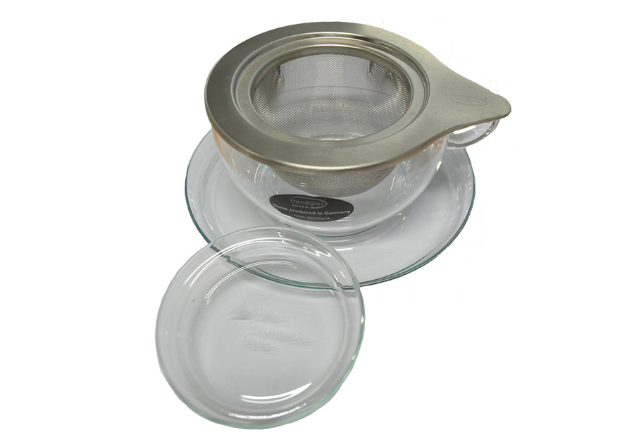 Das Foto zeigt eine gläserne Teetasse mit Teesieb, Untersetzer und gläsernem Deckel.