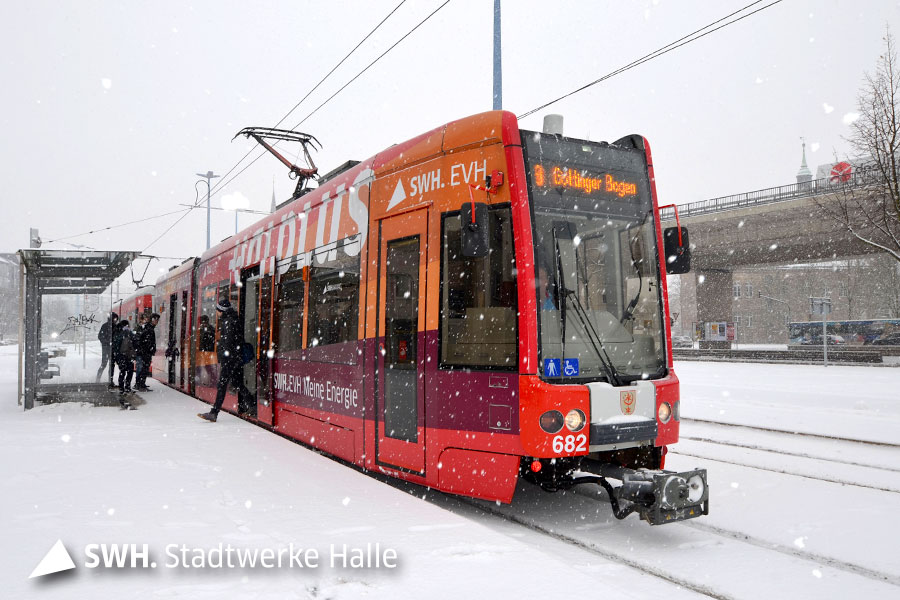 Eine bunt-beklebte Straßenbahn der HAVAG an einer Haltestelle- Fahrgäste steigen aus. Es schneit.