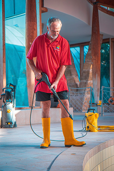 Das Foto zeigt einen Mann in rotem Tshirt mit Maya mare-Logo, Shorts und gelben Gummistiefeln, der mit einem Reiningungsgerät die Bodenfliesen reinigt.