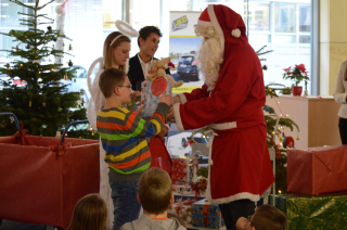 Der Weihnachtsmann übergibt gemeinsam mit seinem Weihnachtsengel einem Kind das Geschenk.