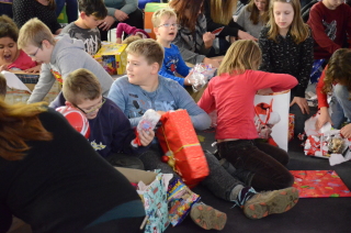 Alle Kinder sitzen auf dem weichen Boden und beginnen, ihre Geschenke auszupacken. Dabei lachen sie.