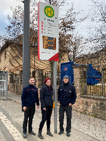 Drei Personen stehen an einer neuen Fahrgastinformationsanlage an einer Straßenbahn-Haltestelle in Halle