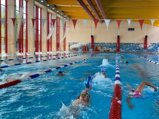 Das Foto zeigt eine Schwimmhalle, in der mehrere Kinder schwimmen.