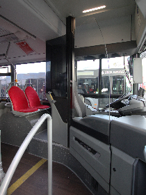 Das Foto wurde von der vorderen Tür eines Busses aufgenommen und zeigt den Innenraum des Busses. Die Fahrerkabine ist mit einer Scheibe von den Fahrgästen abgetrennt.
