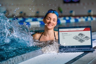 Eine junge Frau präsentiert in der Schwimmhalle im Wasserbecken die neue Webseite der Bäder Halle GmbH auf einem Smartphone.