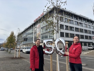 Zwei Stadtwerke Halle-Vertreterinnen stehen vor einem gepflanzten Baum.