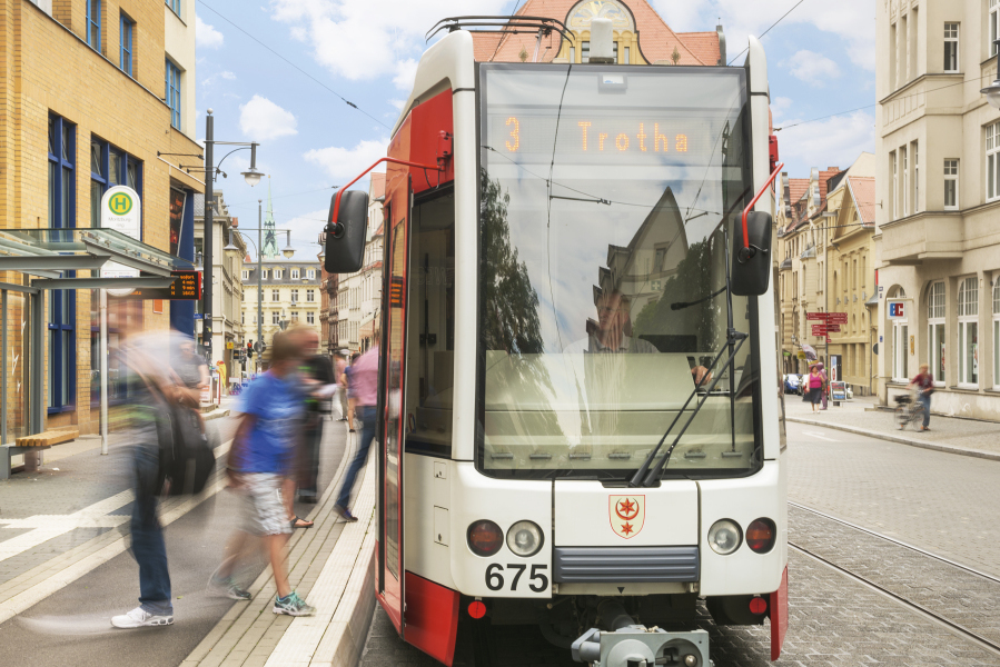 Auf dem Bild ist eine Straßenbahn der Linie 3 mit dem Ziel Trotha abgebildet, die an einer Haltestelle steht und aus der Menschen aus- und andere einsteigen.